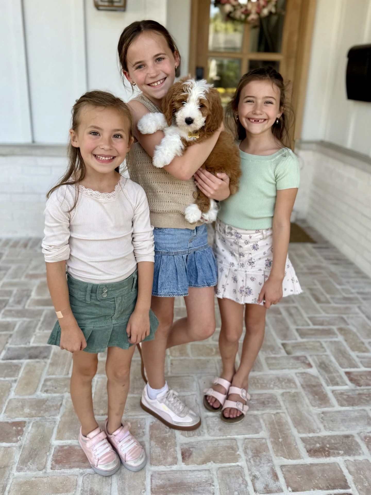 3 sisters holding their Goldendoodle puppy on front porch