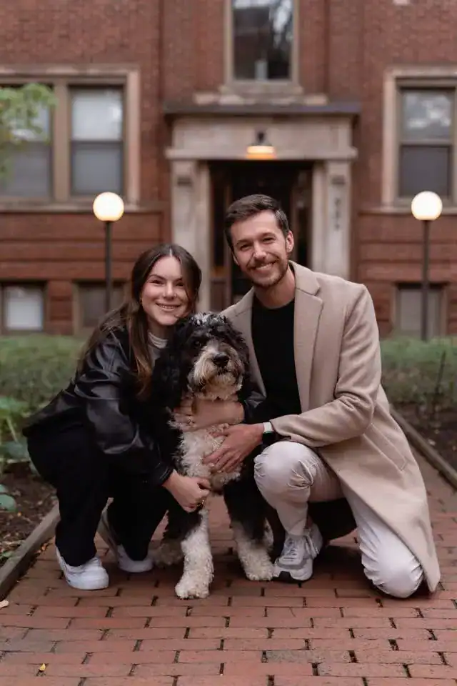 Family posing with their Bernedoodle puppy on brick sidewalk