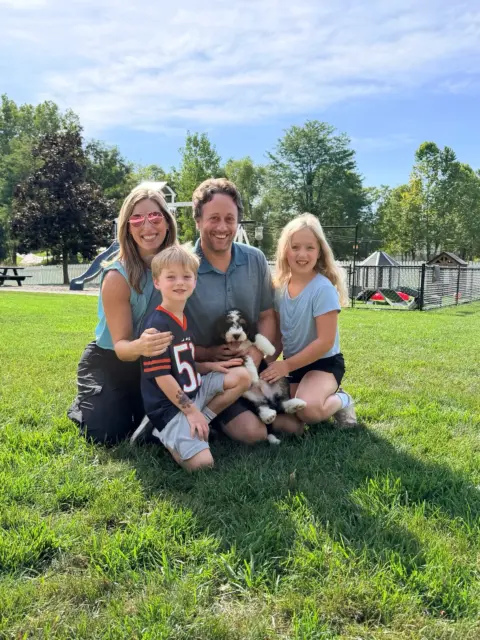 Happy family of four excited to take their new Bernedoodle puppy home.